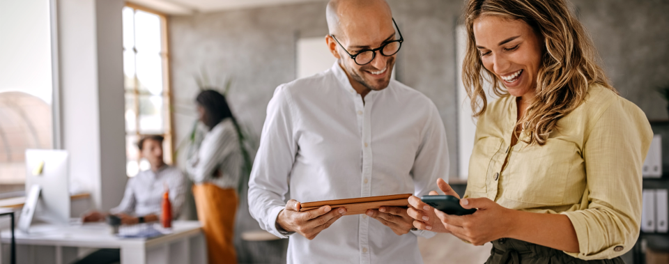 two business professionals smiling while looking at a tablet.