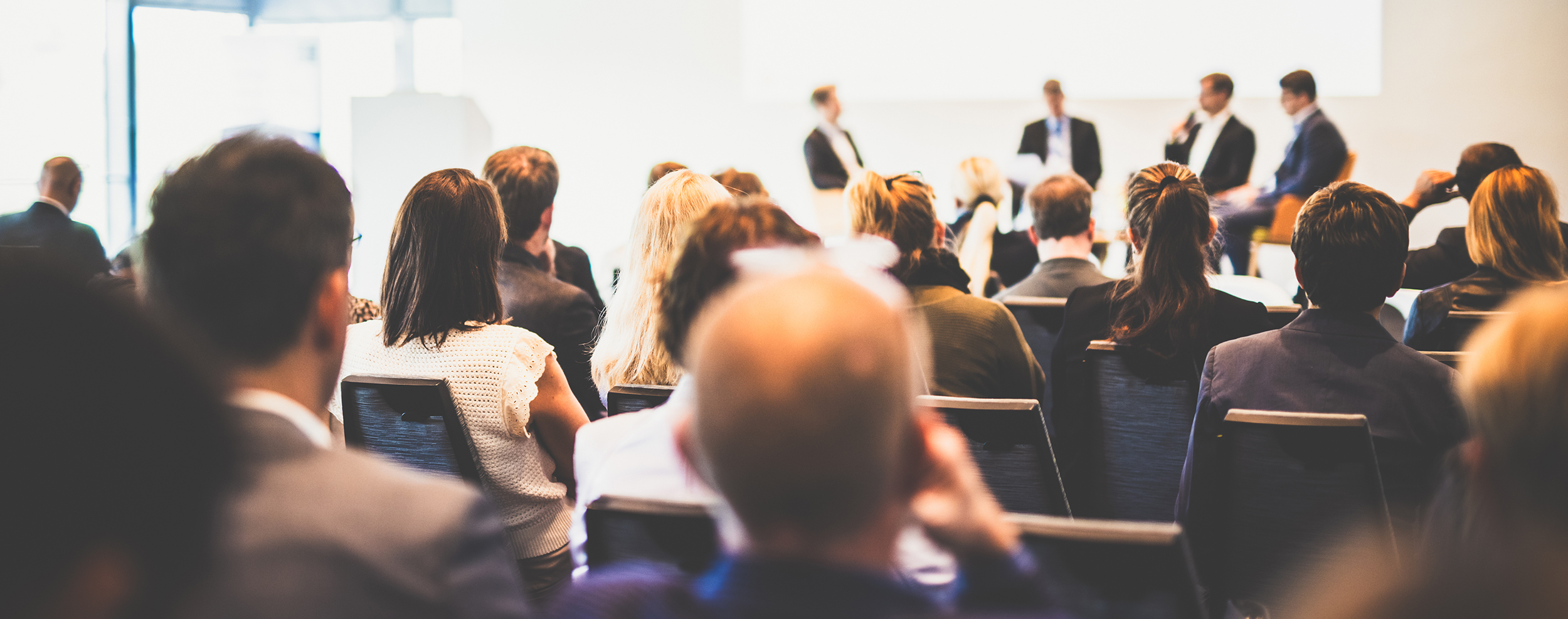 Image of attendees listening to a panel of speakers at a conference