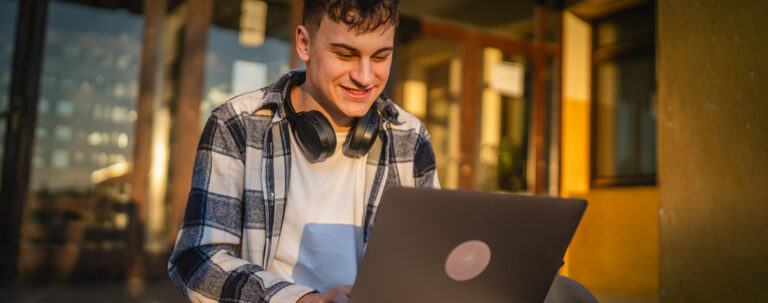 College student working on laptop with headphone around neck